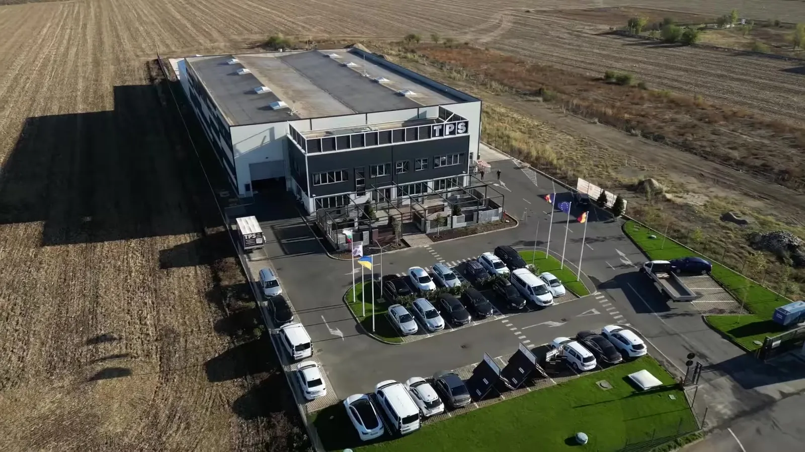 Fabrica TPS de la Popești-Leordeni văzută din dronă: hala, clădirea de birouri cu sigla TPS, showroom-ul de garduri și parcarea